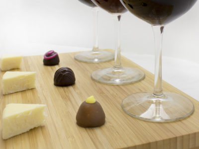 small cheese wedges on a board with chocolate truffles and wine glasses